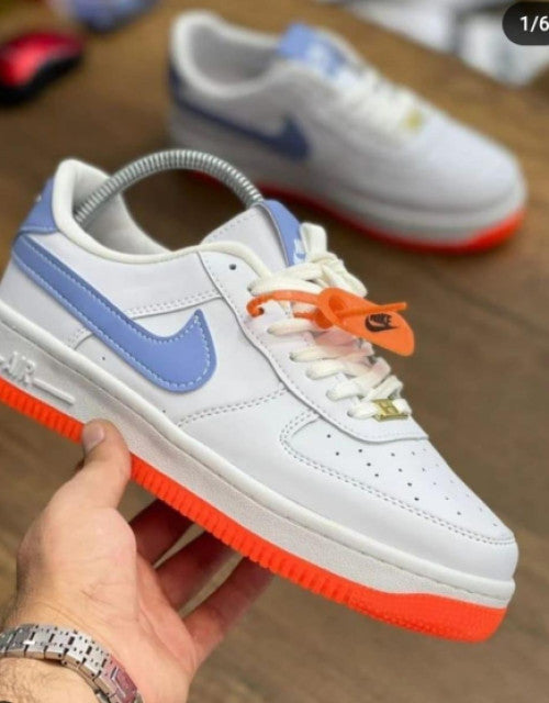 White and blue men's trendy casual shoes with orange sole and Nike branding held in hand on wooden floor
