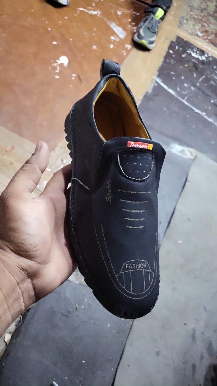Black men leather casual shoes with slip-on design and stitched detailing held in hand