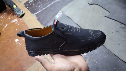 Black men leather casual shoes with stitched detailing held in hand on workshop floor