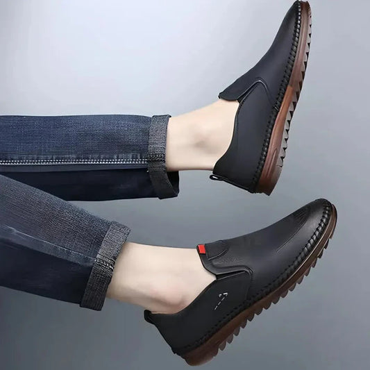 Men's black casual shoes with brown textured soles worn with rolled-up dark jeans