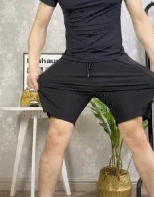 Man wearing black men's cotton polyester shorts stretching fabric while standing indoors
