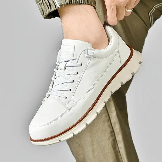 White men's soft sole sneakers with brown trim and lace-up design, worn with olive pants
