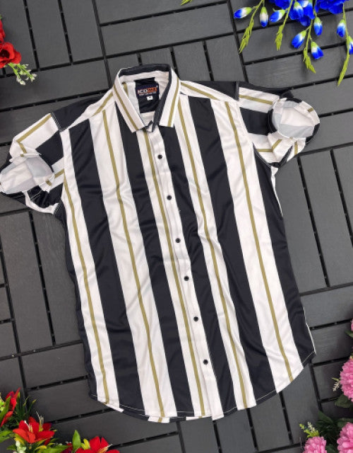 Black white and beige men's striped casual shirt laid flat on a dark gray wooden surface surrounded by flowers