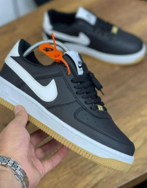 Black and white Nike sneakers held in hand showcasing trendy men's footwear online with gum sole and lace-up design