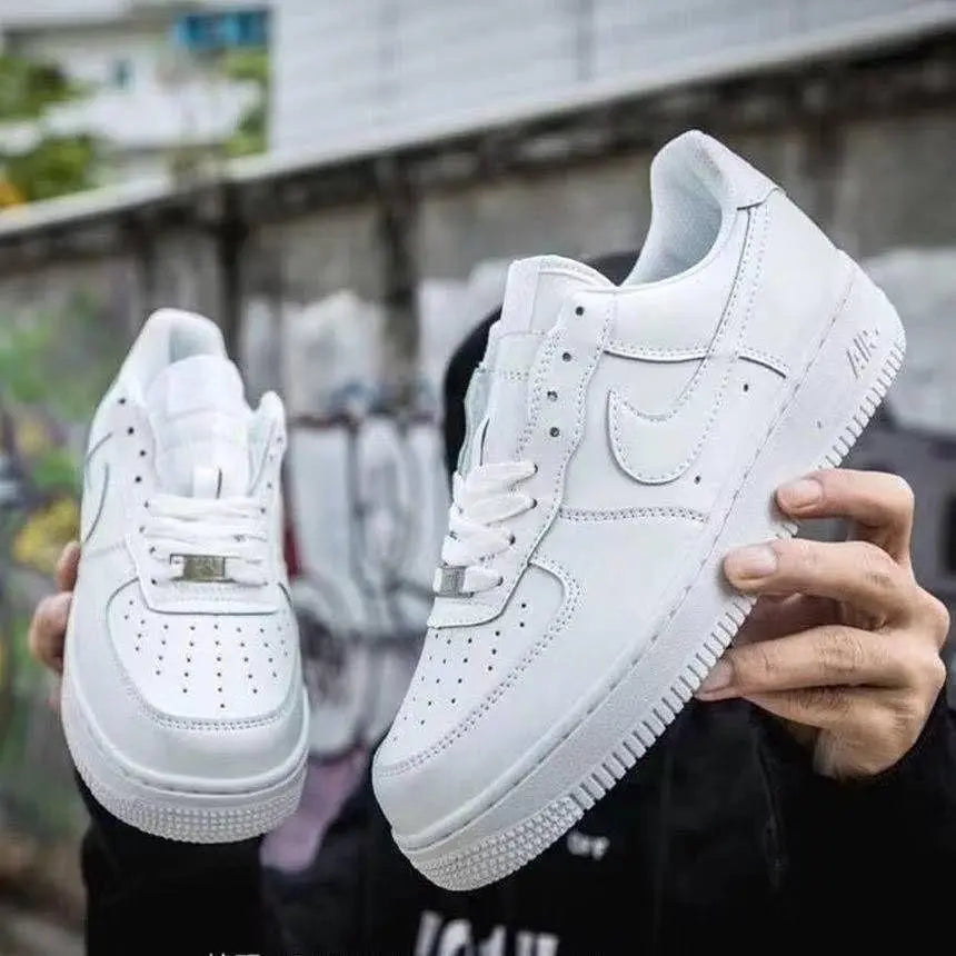 Mens white casual shoes held outdoors featuring classic perforated design and clean stitching