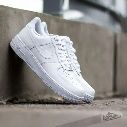 Men's white casual shoes with lace-up design and rubber sole resting against a concrete wall