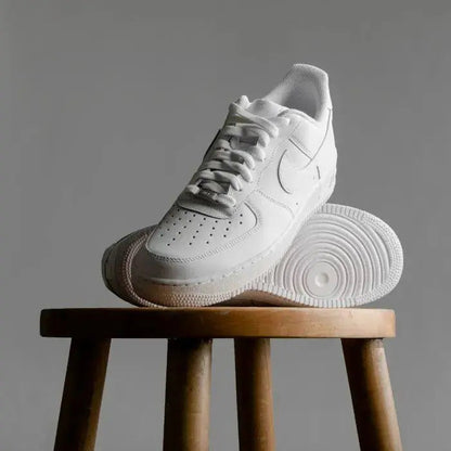 Men's white casual shoes with lace-up design and rubber sole placed on wooden stool