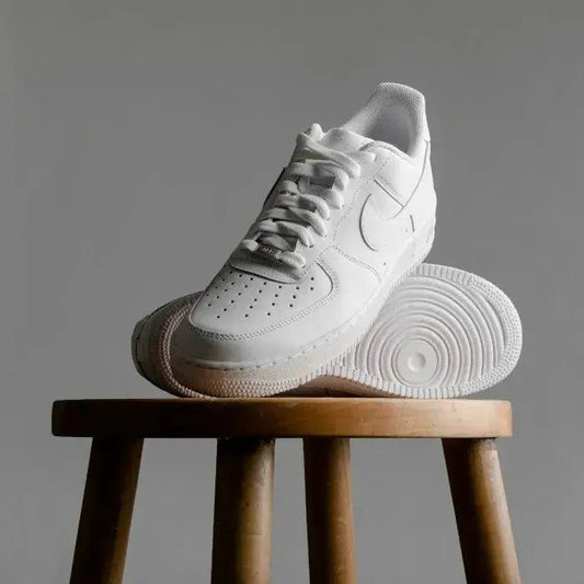 Men's white casual shoes with lace-up design and rubber sole placed on wooden stool