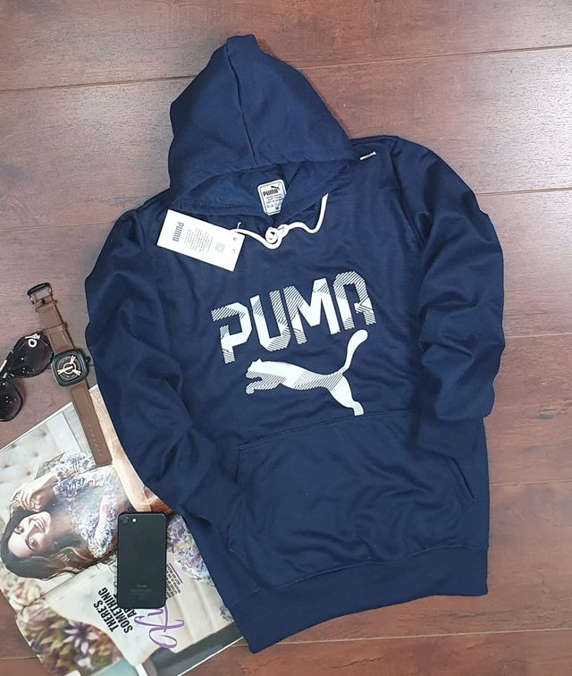 Navy blue Puma hoodie for men and women laid flat on wooden floor with sunglasses, watch, phone, and magazine