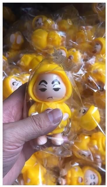 Hand holding a yellow Shinchan face changing keychain with multiple similar keychains in background