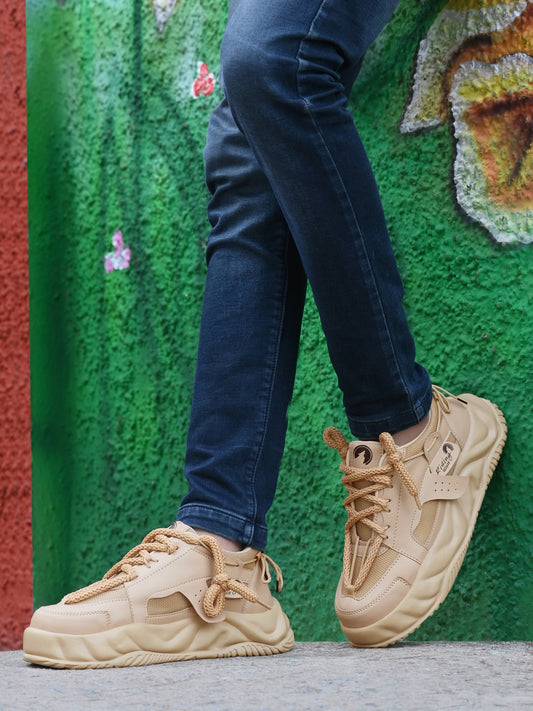 Tan sport shoes for men worn with dark blue jeans against a colorful textured wall background