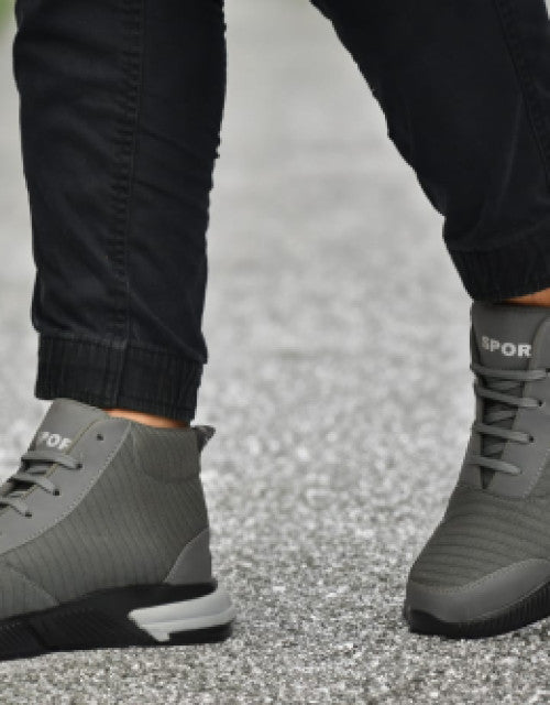 Gray sporty trendy men's sneakers India worn with black pants on asphalt surface