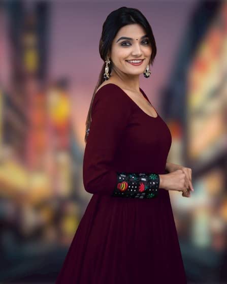 Woman wearing a maroon women's rayon full sleeve gown with embroidered cuffs standing in a blurred cityscape